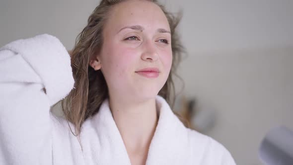 Closeup Portrait of Happy Smiling Young Beautiful Woman Drying Hair in Slow Motion with Hair Dryer alt