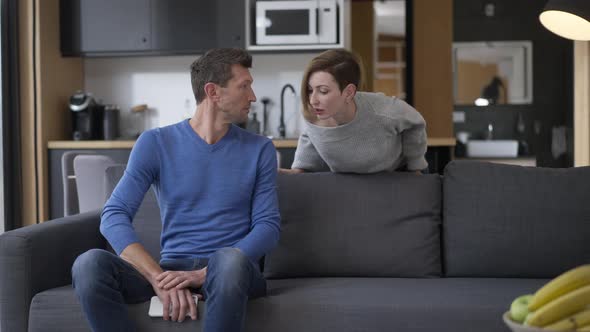 Guilty Husband Hiding Smartphone As Wife Talking to Spouse in Living Room at Home alt