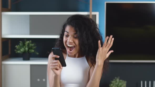 Excited Young African American Woman Rejoices at Message on Her Smartphone. Happy Female Looking at alt