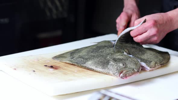 Fish vendor cutting a turbot for the clients, with black background alt
