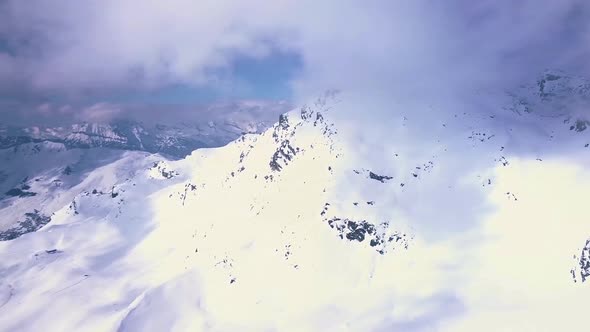 Aerial drone shot of bright white snow and mountains covered in clouds above the ski resort town of alt