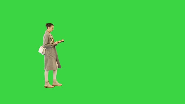 Young Woman in Stylish Clothes Walks with a Book Stops and Closes It on a Green Screen Chroma Key alt