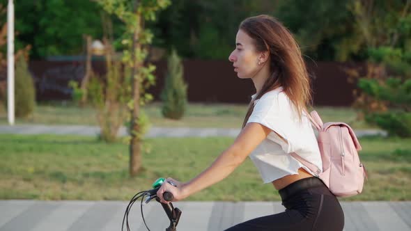 Beautiful young woman rides a bicycle in a city park on a sunny summer day. Slow motion. alt