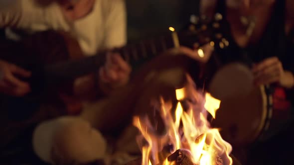 Friends Speaking Smiling Playing on Instruments Sitting Near Bonfire at Night Beach alt