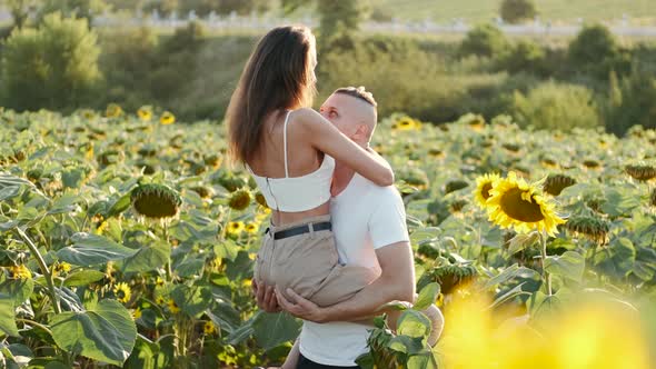 Young Loving Man Holding His Girlfriend in Hands Among Sunflower Plantation alt