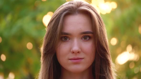 Outdoors portrait of beautiful young brown-haired woman looking at camera.