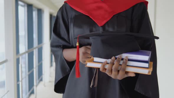 African American Female Graduate in Mantle Stands with a Books and Hat in Her Hands alt