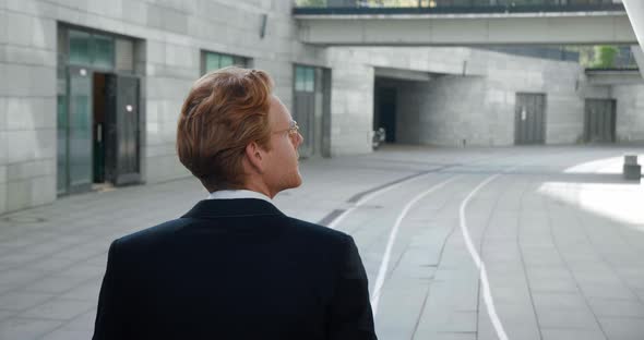 Back View of Caucasian Redhaired Businessman Walking Outdoors the Street at Downtown alt