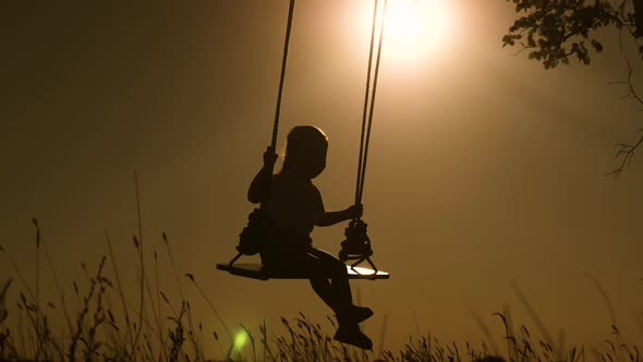Baby and Mom Swinging on a Swing in Park in Sun. Silhouette of Small Healthy Child on Swing alt