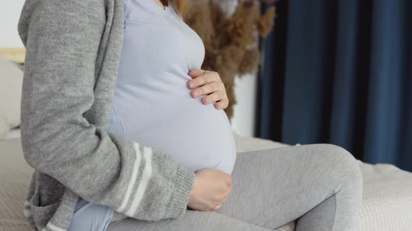 Close Up of Pregnant Woman in Home Clothes Sitting on a Double Bed alt