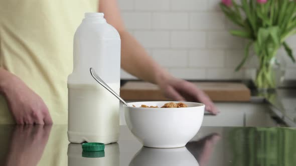 Woman pouring milk onto breakfast cereal alt