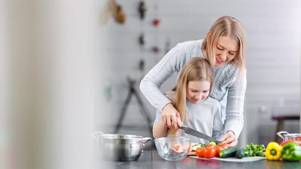 Pretty Mother is Teaching Her Daughter to Cut Vegetables with a Sharp Knife alt