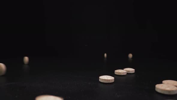 Throwing Small Beige Drug Pills To Pile on Black Surface alt