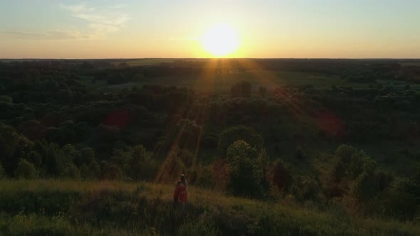 Aerial View Mother and Son Standing on Mountain Cliff Hugging Watching Sunset alt