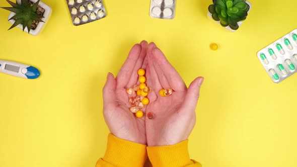 The palms of a young woman hold a lot of pills and vitamins for human health on a yellow background
