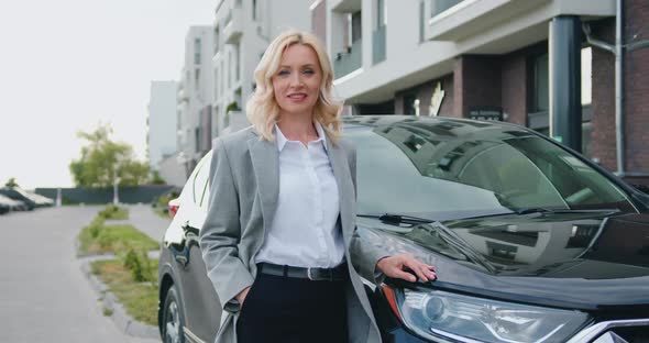 Businesswoman Standing Near Parked Car in the Parking Look at Camera Smiling alt