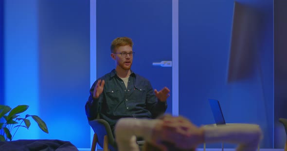 Young Man Sits in a Chair on a Talk Show Emotionally Talking and Gesticulating