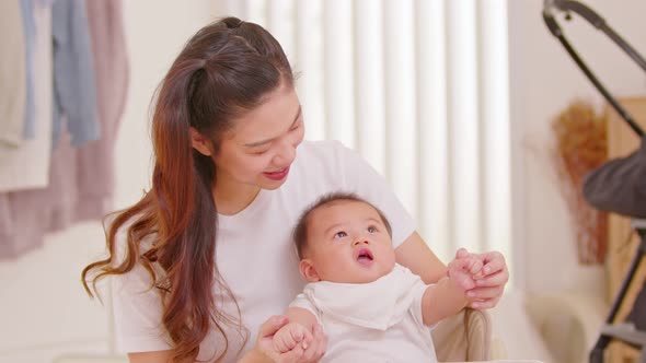 New asian mom playing to adorable newborn baby on chair smiling and happiness at home.Happy Mother t alt