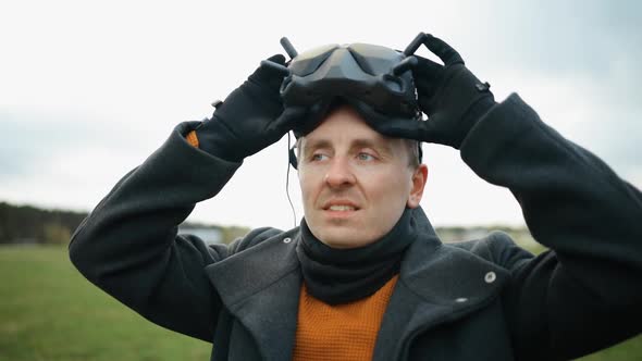 Serious Man Puts on Black FPV Drone Goggles Outdoors alt
