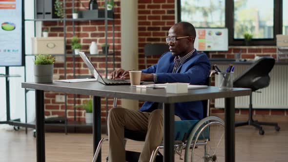 Paralyzed Employee in Wheelchair Using Laptop to Plan Project alt