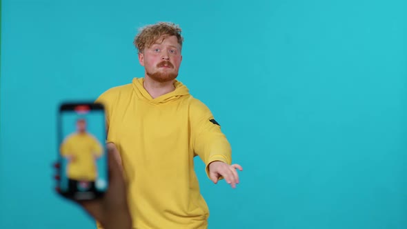 Young Guy in Yellow Hoodie Dances to the Music on a Blue Background and Takes a Selfie Video on alt