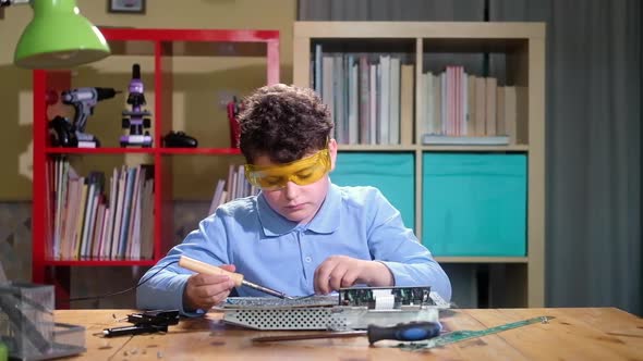 Child cute schoolboy at desk with tools is studying Electronics and repairing