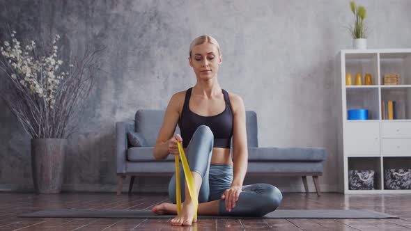 Young and sporty girl in sportswear is doing exercises in home interior using resistance band. alt