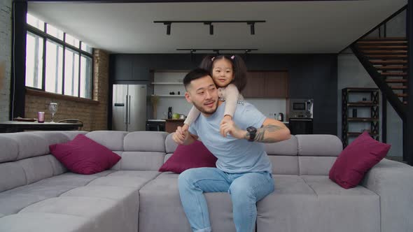 Happy Asian Dad and Toddler Daughter Having Fun on Sofa alt