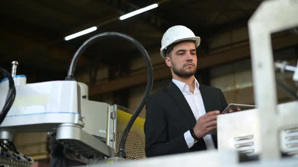 A young plant manager controls the machine's process and takes notes on a tablet alt