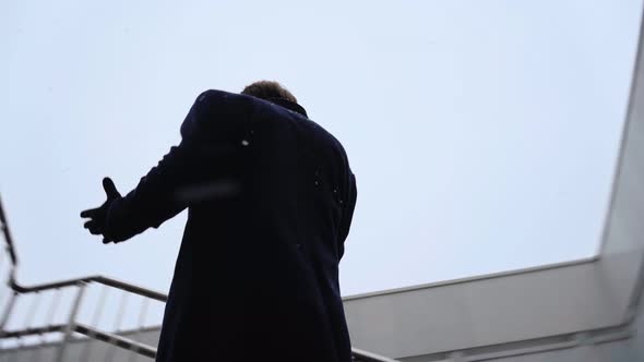 Young Businessman Speaks on Mobile Phone Near Business Center During Snowfall alt