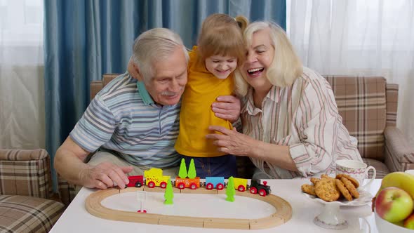 Child Girl Kid Involved in Build Board Game Ride Toy Train on Railroad with Senior Grandparents Home alt