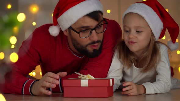 Father and Girl Open Gift Box with Magic Light at Dark Next to Christmas Tree alt
