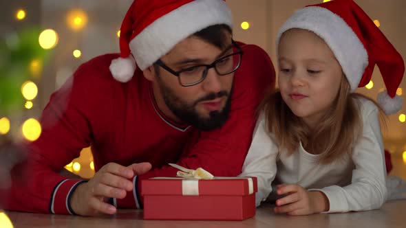 Father and Girl Open Gift Box with Magic Light at Dark Next to Christmas Tree