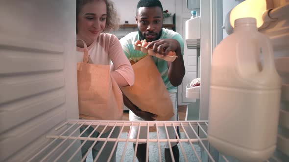 Multiethnic Couple Unpacking Groceries in Fridge at Home alt