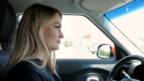 Blonde Young Woman is Driving a Car in the City alt