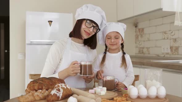 Cute Girl and Her Mom with Faces Smeared with Flour Drinking Hot Cocoa with Marshmellow alt