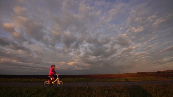 Little girl rides a bicycle rides on a scenic rural road at sunset