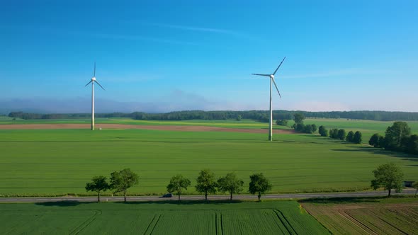 Wind Turbines generating electricity over lush farmlands. Aerial. alt