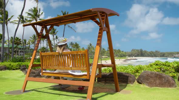 Back View of Elegant Lady Swinging on Wooden Swing Luxury Resort at Ocean Beach alt