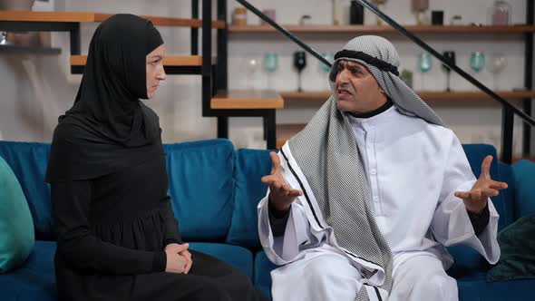 Irritated Annoyed Middle Eastern Man in Traditional Clothing Arguing with Dissatisfied Woman Sitting alt