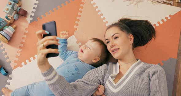Young Attractive Mom Lies on Floor with Son Dressed in a Blue Bodysuit Boy Looks alt
