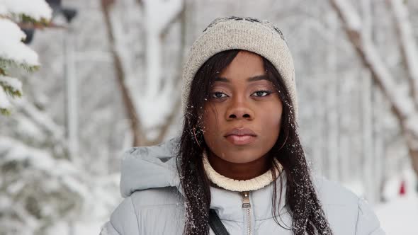 Young Black Woman in White Jacket Stands in Winter Forest and Smiles to the Camera alt