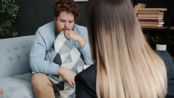 Sad and Nervous Man Speaking to Psychologist Sharing Feelings Sitting on Couch Hugging Pillow alt