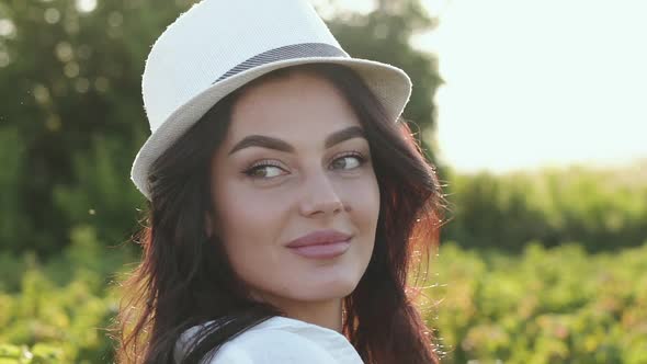 Charming Brunette in Hat Smiling Looking Around and at Camera in Field alt