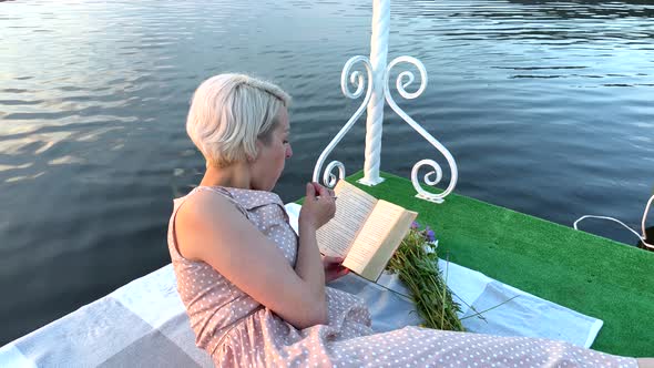 A Girl on a Raft Eats a Berry and Reads a Book