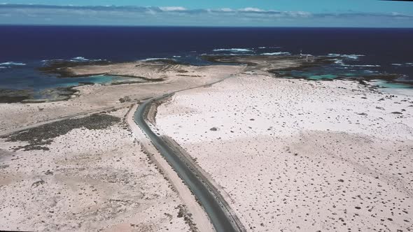 Above view of black asphalt road with desert and sand dunes around - coastline with blue ocean alt