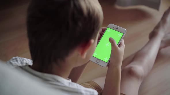 Small boy watching content on phone. Green screen mock-up. Back view of kid with smartphone