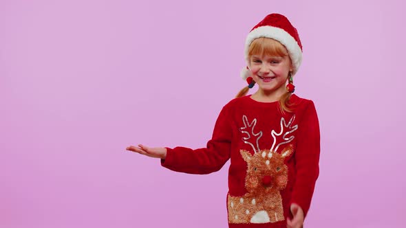 Girl Child in Christmas Sweater Deer Showing Thumbs Up and Pointing at on Blank Advertisement Space alt