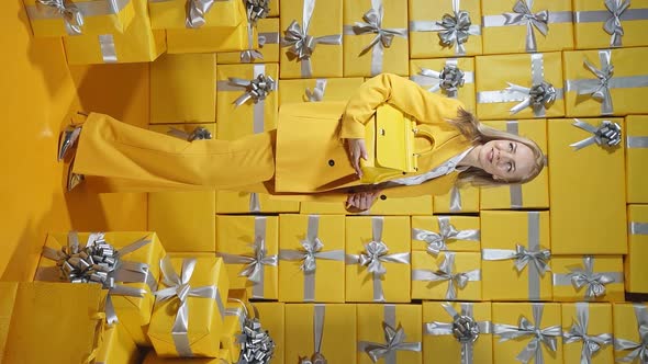 An Attractive Blonde in a Yellow Suit and a Yellow Purse in Her Hands Poses Against the Background