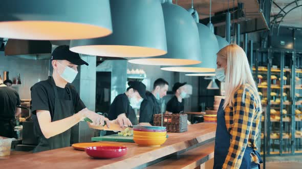 Waitress in a Face Mask Gets an Ordered Dish at the Counter alt